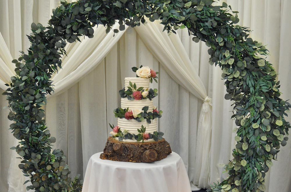 Floral Moon arch with foliage to frame a wedding cake at De Vere Cotswold Water Park Hotel
